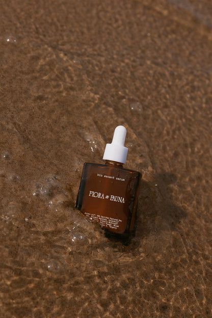 Brown rectangular bottle of Bio Escent Serum in the sand and water. 