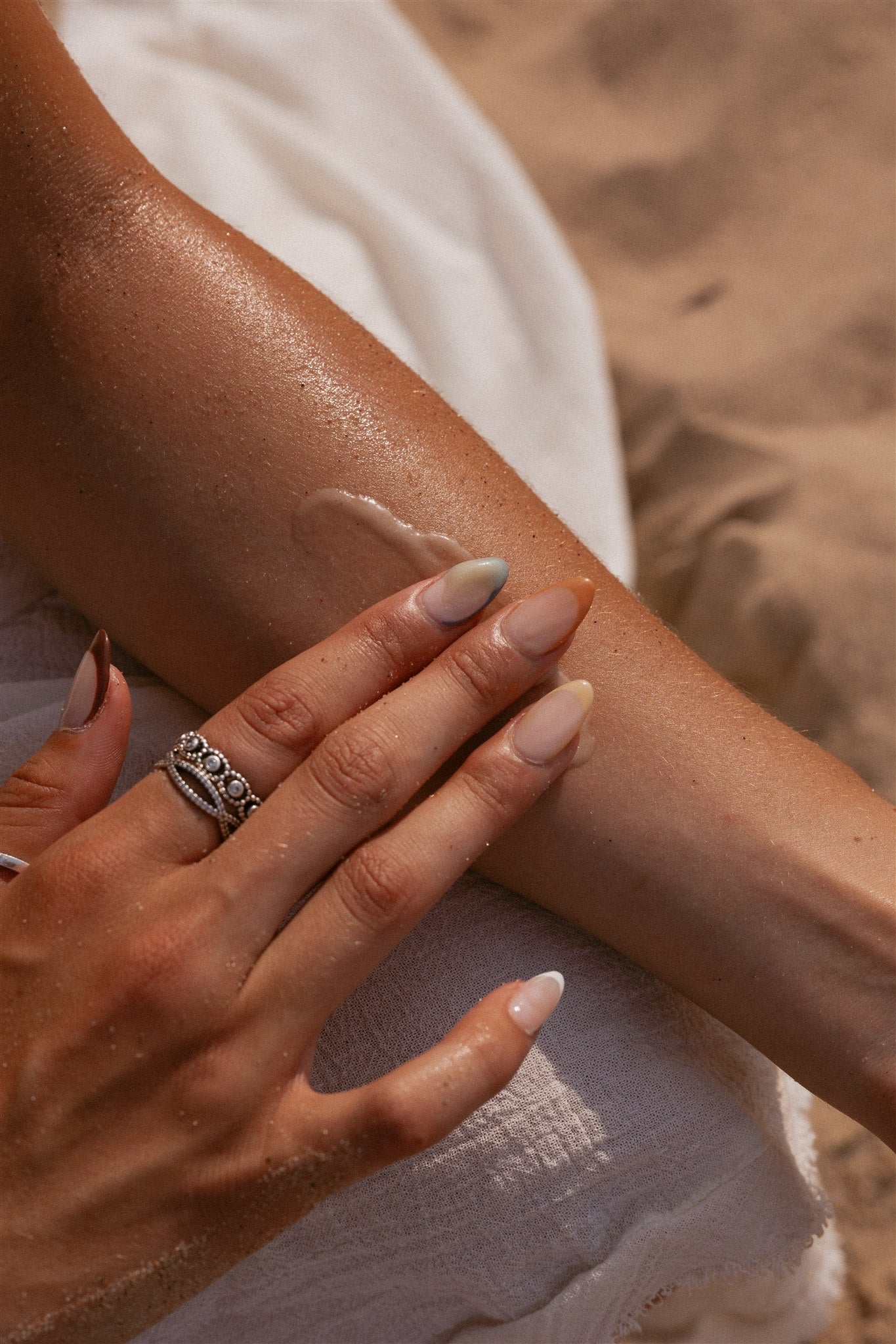 Girl at the beach applying cream to inside of her arm.