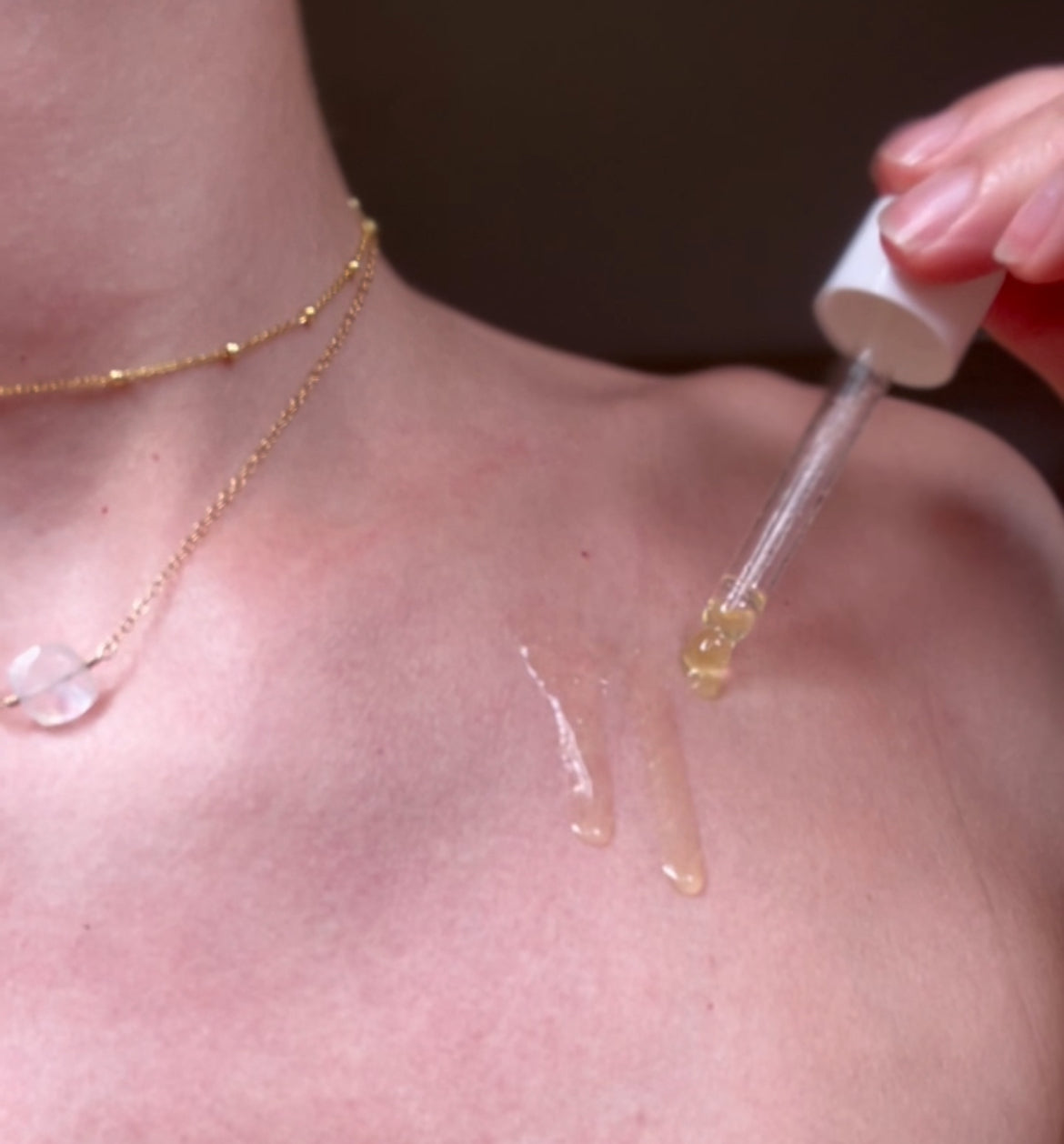 A girl holding a dropper with oil in it, applying three drops onto her skin. 
