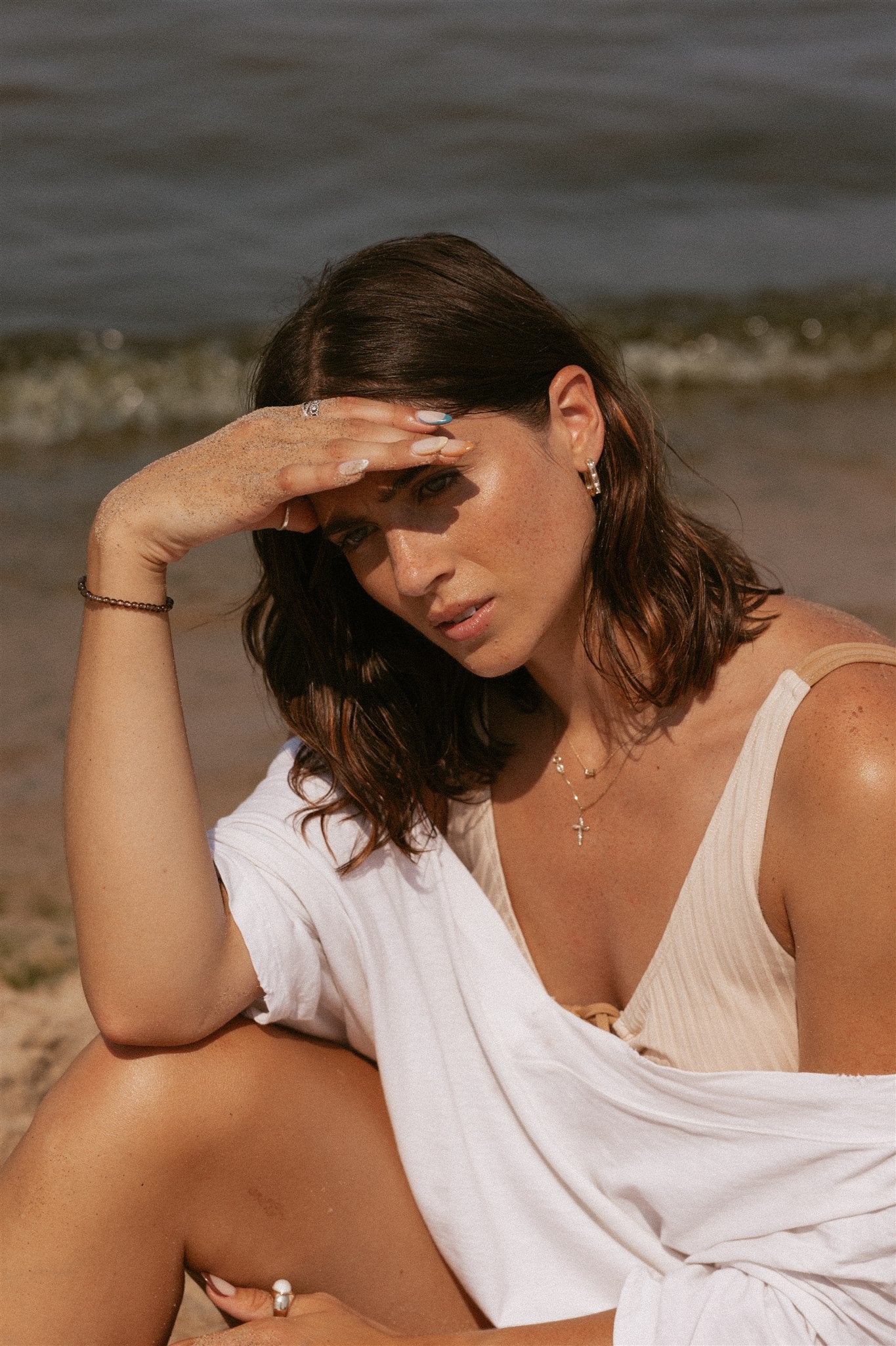 Girl sitting on beach facing the sun while holding hand as a visor above her eyes.