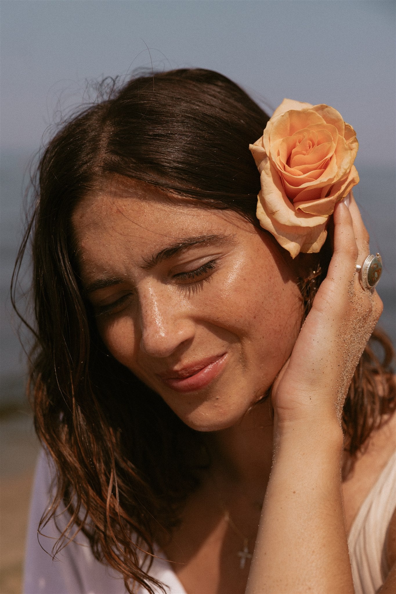 Girl smiling with her eyes closed and holding a rose above her ear in her hair. 