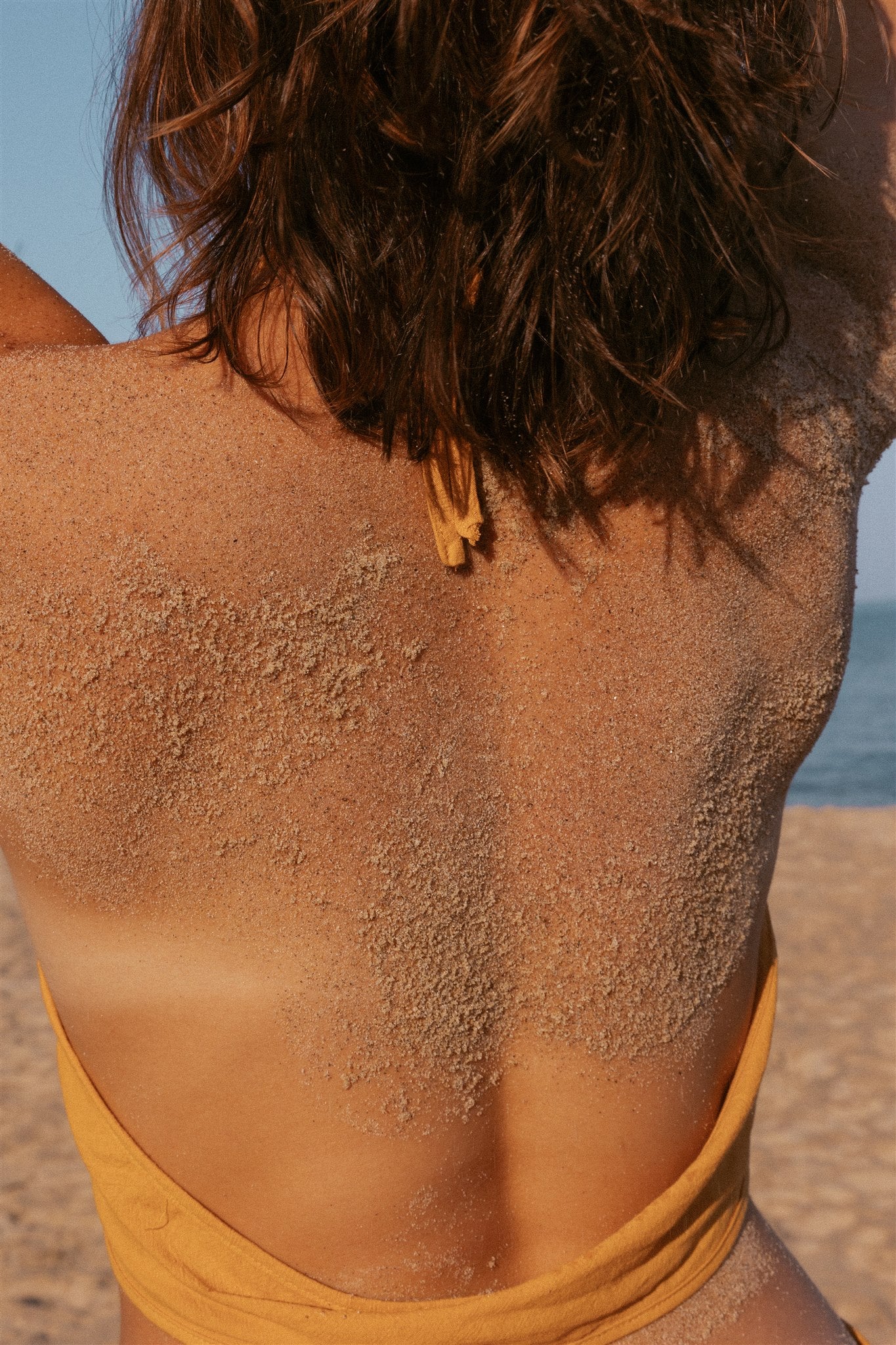 Close up photo of a girl's sandy back in the sun, wearing a low back yellow dress. 