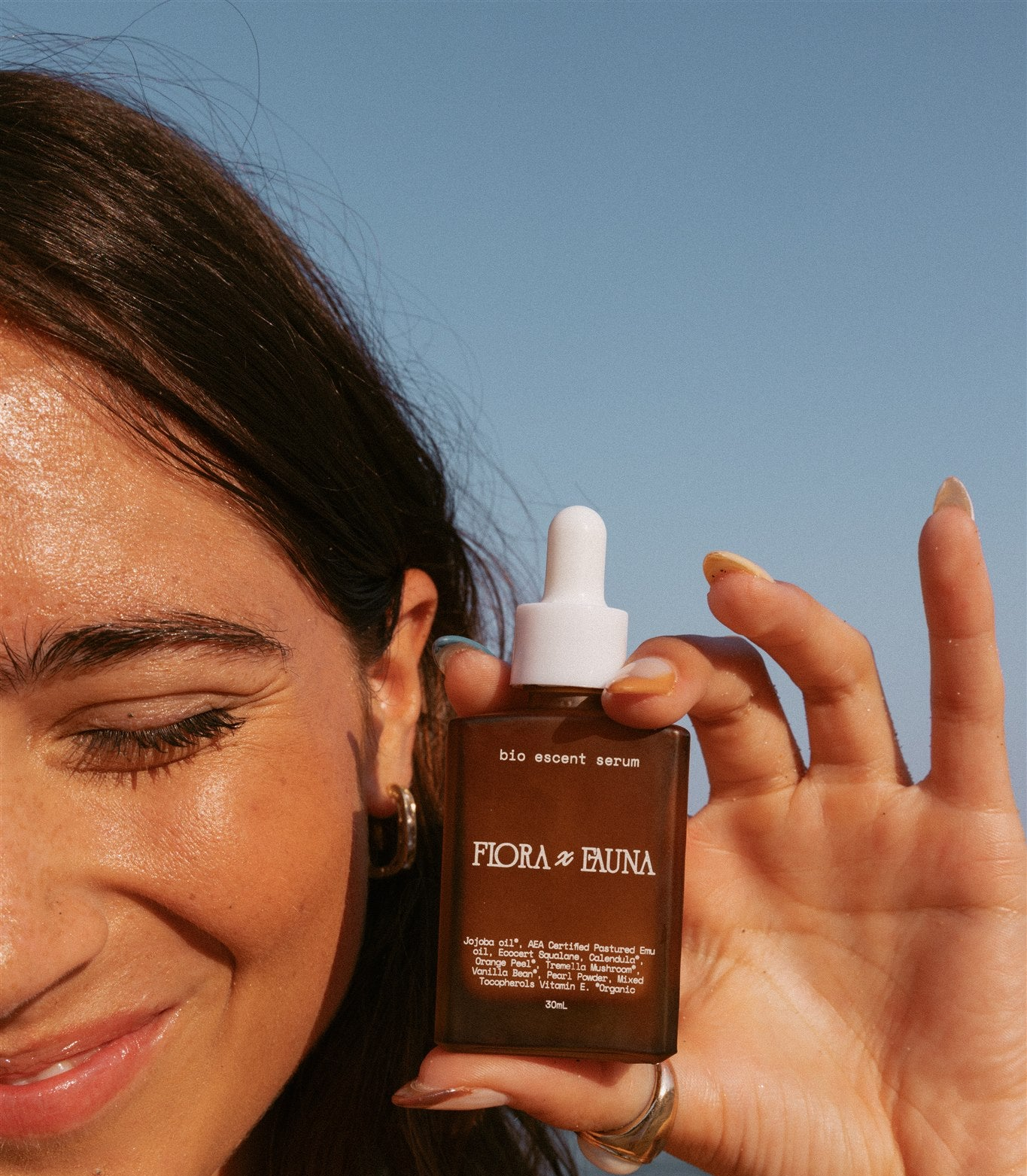 Girl smiling with eyes closed holding serum bottle next to her face. 