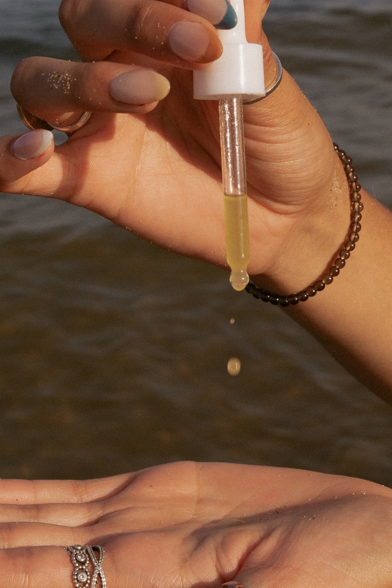 Using glass dropper to drip serum into palm of hand over the lake. 