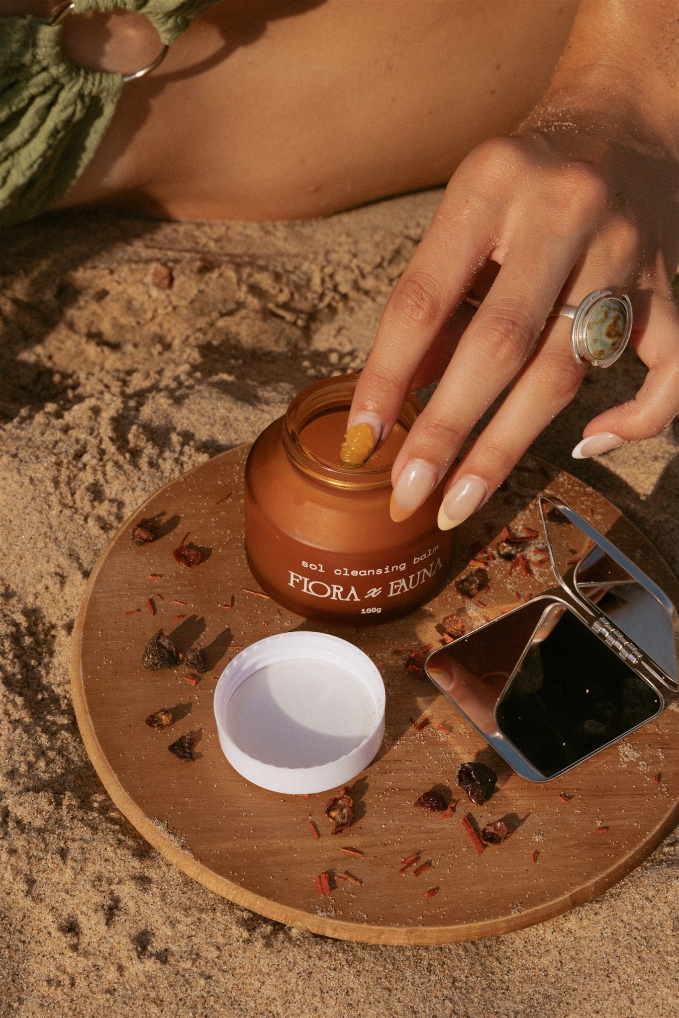 Girl dipping finger into sol cleansing balm on wooden tray over the sand. 