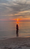 Video of girl walking in the water away from the camera, towards the sunset. 